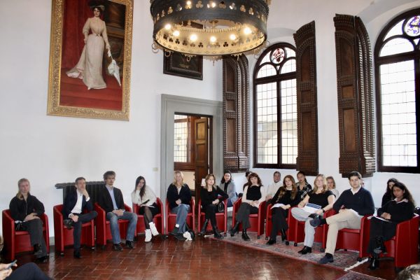 A large group of students and professionals seated in a circle for a round table discussion in a historic hall at ESE Florence.