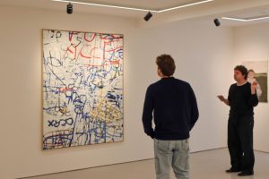 Dos hombres mirando un lienzo con marcas abstractas rojas y azules.