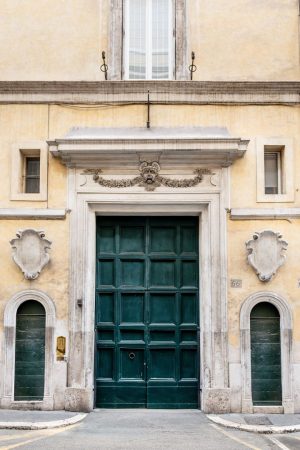 Fachada de un edificio histórico con un gran portón central verde, un mascarón esculpido y dos entradas laterales menores.