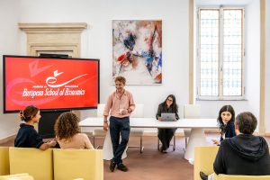 Students interacting in a university classroom with a screen in the background showing the European School of Economics logo.