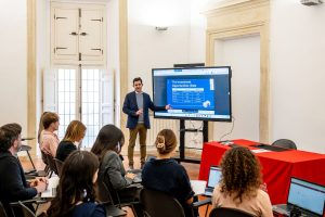 Docente che tiene una lezione con uno schermo che mostra la presentazione The Investment Opportunities davanti agli studenti.